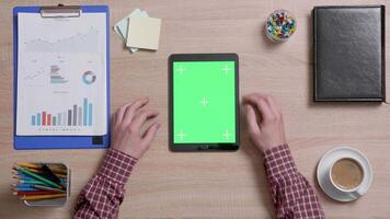 Top view of male hands scrolling on the right edge of a green screen on a black tablet. Tracking motion. Office wooden desk. Corporate concept. Chroma key. video