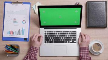 Top view of man's hands while he looks at the green screen of his laptop. Office environment concept. Working indoors with coffee. video