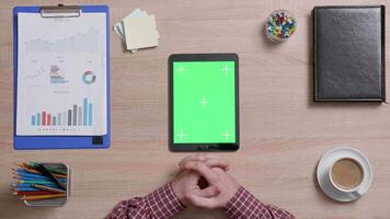 Top view of male hands looking at a green screen of a black tablet. Tracking motion. Office wooden desk. Corporate concept. Chroma key. video