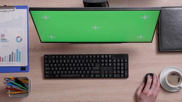 Top view of a man working on his computer with green screen on his monitor. Office environment concept. Working indoors with coffee. video