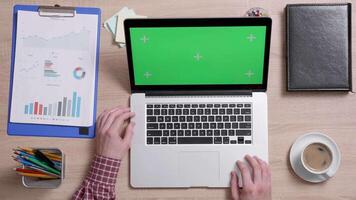 Above shot of male hands using the touch pad of his laptop with green screen on. Office environment concept. Working indoors with coffee. video