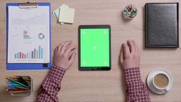 Top view of male hands scrolling on the bottom edge of a green screen on a black tablet. Tracking motion. Office wooden desk. Corporate concept. Chroma key. video