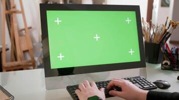 Male hands typing a text on the keyboard in front of a green screen. Young painter works on his computer in a creative workshop. video