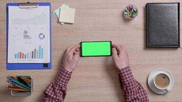 Man's hands over a office desk holding smart phone with green screen. Business and finance office concept. Chroma Key. video