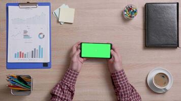 homme mains plus de une Bureau bureau départ à jouer une Jeu sur une intelligent téléphone avec vert filtrer. Bureau travail concept. au dessus coup de une en bois bureau. video