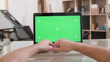 Man working in a artsy workshop in front of a green screen. Pov of typing at a laptop with green screen on. video