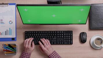 Top view of male hands typing on a keyboard in front of a green screen monitor. Office concept. Man working indoors. Corporate employee. video