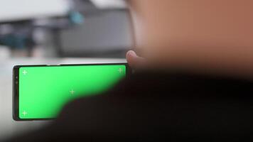 Revealing over the shoulder shot of a green screen on a smartphone. Man holds his phone horizontally and keeps watching. video