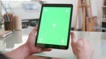 Man holds a black tablet with green screen on in both hands and keeps watching. Designer looking at sketches in his studio. Chroma key close-up shot. video