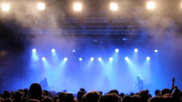 Fans watch their favorite music band performing on the stage. Bright lights on their heads. Shot from behind a crowd. video