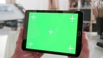 Holding a tablet with green screen on in a artists workshop. Male hands holding horizontally ablack tablet. Looking at a green screen. video