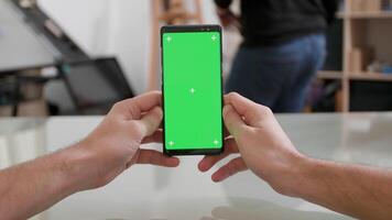 mans punt van visie Holding een smartphone verticaal met groen scherm Aan. aan het kijken een video Aan th internet gedurende een pauze.