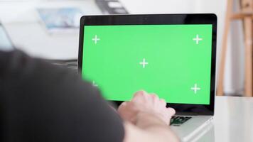 Over the shoulder shot of a man working at his laptop in an office. Green screen concept. Man in black t-shirt typing at his computer. video