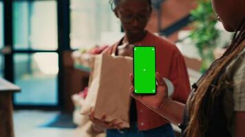 handelaar Holding smartphone met groene scherm Scherm Bij boeren markt, presenteren geïsoleerd Chroma sleutel mockup Aan scherm. vrouw klein bedrijf eigenaar gebruik makend van copyspace lay-out Aan telefoon. video