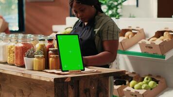 Device showing greenscreen template at local supermarket, tablet placed on store counter next to additives free sauces and pantry supplies in reusable jars. Merchant displaying copyspace screen. video