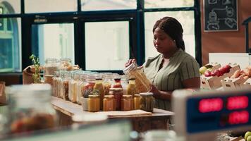 Vegan shopper looking at homemade sauces or dressings to buy additives free bulk products from local zero waste eco store. Woman examining jars with pasta or spices, ecological goods. video