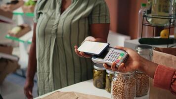 cliente comprando Produce utilizando nfc móvil pago a posición, yendo tienda de comestibles compras para de cosecha propia frutas y verduras. vendedor ponderación bienes en escala a efectivo registro, agricultura concepto. Mano disparo. video