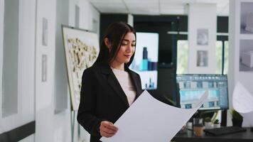 Asian architect studying blueprint papers in creative agency, examining building model on desk. Technician looking at property floor plan to design new home for clients, 3d maquette. video