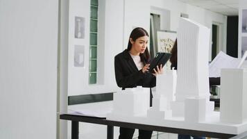 grafisch artiest ontwikkelen bouwkundig 3d gebouw, vergelijken blauwdrukken van papieren met schaal tocht Aan tablet. creatief ingenieur werken Bij coworking ruimte klein bedrijf, architectuur bureau. video