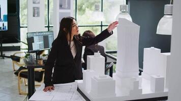 Architecture office employee looking at building model, working with printed project blueprints. Architect analyzing draft on house outline in coworking space, real estate agency worker. video