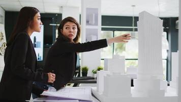 Cad experts examining architectural blueprints at agency, holding 3d printed building model to measure elements and shapes. Team of women architects studying property scale draft, coworking space. video