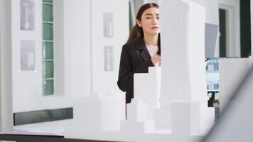 Developer working with laptop to gather scale elements, looking at 3d printed model of building maquette. Technician reviewing creative architectural plan for new construction project. video