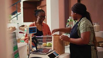 comerciante utilizando escala a peso frutas y verduras para cliente, relleno en bolso con pesticidas gratis comestibles. comprador comprando éticamente de origen de cosecha propia Produce desde local eco almacenar. Mano disparo. video