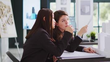 Developers trying to design blueprints for new construction site, working together to draw lines and create architectural drafts for project. Technicians examine 3d printed models at workstation. video