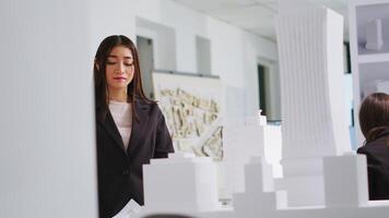 Bij ontwerp tafel, ingenieur beoordelingen schema's en 3d bouw plannen in bestellen naar ontwikkelen fabricage lay-out voor stedelijk behuizing project. vrouw evalueert maten en componenten. handheld schot. video