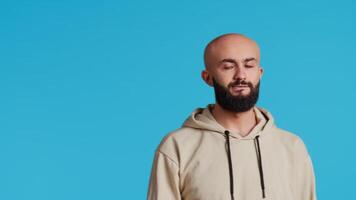 Middle eastern guy welcoming people in studio with a wave, saying hello and smiling over blue background. Arabic person waving and greeting friends, posing with confidence. Camera 2. video