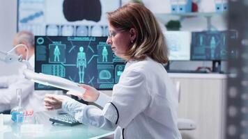 Female scientist uses a magnifying glass in modern laboratory. She carefully examines a sample while her team works in the background video