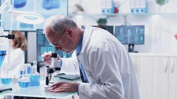 In modern research facility mature chemist is taking notes after studying a sample using the microscope video