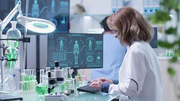 Adult biologist workign in modern laboratory. She is typing on computer that displays a modern and advanced human scan video