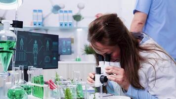 Revealing shot of female scientist looking into the microscope in modern laboratory video