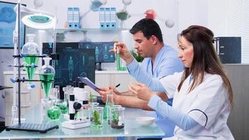 Scientists with her assistant looking at test samples with green liquid in busy modern laboratory video