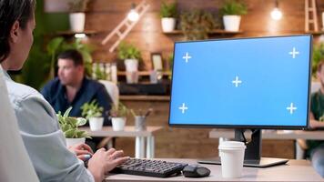Woman typing on a computer with a blue screen mock-up in modern and cozy office video