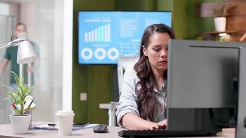 Revealing shot of a busy office with people working in it. A woman in casual clothes sips coffee and types on the computer video