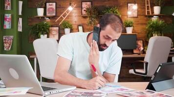 giovane soddisfare Creatore parlando su il Telefono e scrittura Appunti. Lavorando su un' nuovo progetto. video