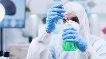 Close up static shot of biotechnologist in coverall pouring green liquid on plants in modern and high-end research center video