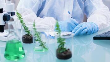 Close up footage of biologist desk making notest in a clipboard next to plant and test tubes. Dolly shot video