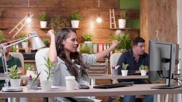 Female manager dances happily at her desk while her colleagues are working in the background. Slow motion medium shot video