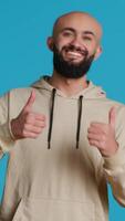 Vertical Video Middle eastern person giving thumbs up on camera, feeling cheerful and showing his approval. Arab adult doing okay or like symbol in studio, expressing positivity and agreement. Camera 1.