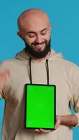 Vertical Video Muslim person holding tablet with greenscreen template, presenting isolated copyspace on device display. Middle eastern guy using gadget to create commercial ad with chromakey. Camera 1.