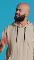 Vertical Video Arab male model doing no symbol on blue backdrop, showing his rejection and denial in studio. Middle eastern guy expressing refusal with a negative gesture, serious man. Camera 1.