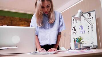 Beautiful young blonde fashion designer looking at her latest designs. Woman in design production. video