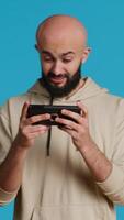 Vertical Video Joyful muslim man playing mobile video games in studio, enjoying online competition using smartphone app. Arabic gamer having fun with roleplaying challenge contest. Camera 1.