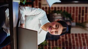 Vertical video Zoom in on joyful asian employee writing important emails at computer desk, finalizing deal with business partners. Portrait close up shot of happy employee typing on laptop, camera B