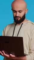 Vertical Video Middle eastern man works with cyber security on laptop, trying to do some software programming and report bugs. Young adult operating as a system developer in studio. Camera 2. Handheld shot.