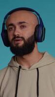 verticale vidéo milieu est ayant amusement écoute à la musique sur casque, dansant autour dans studio et profiter moderne Chansons sur radio. arabe la personne sentiment détendu et insouciant avec airs. caméra 2. video