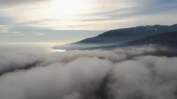 Top view of mountain landscape with low clouds and blue sky. Shot. Beautiful landscape protruding from clouds of mountains against of sea horizon with reflection of bright sunlight video